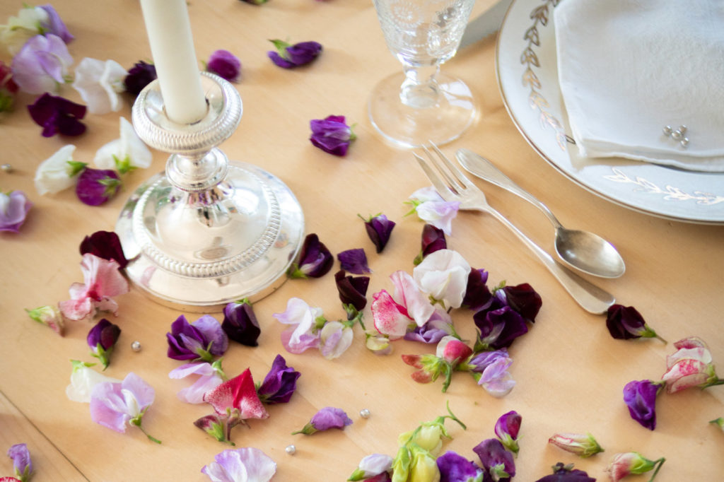 Pétales de fleurs dans les tons violets, posés sur une table avec de jolis couverts