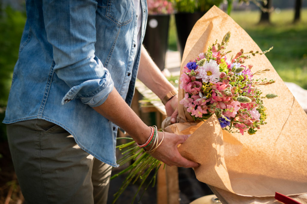 Mains d'une femme emballant des fleurs dans un papier kraft pour en faire un bouquet fait main